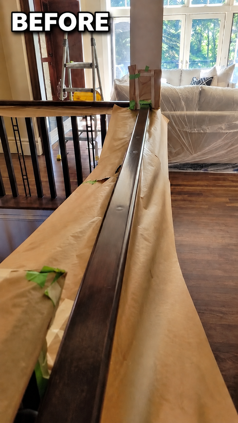 Original dark wood railing before refinishing, with nearby furniture protected for the work